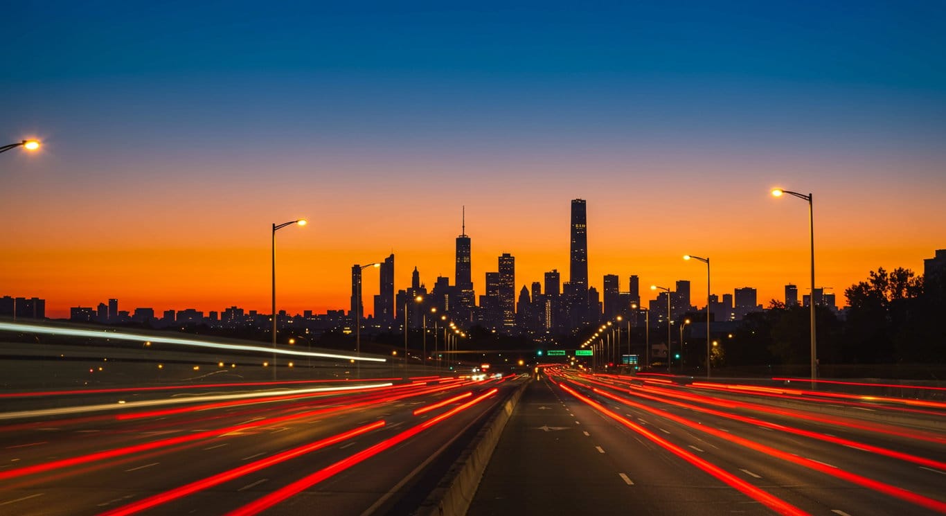 Cityscape at dusk with blurred cars, representing modern urban transportation.